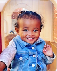 a little girl in a denim jacket smiling in a playhouse