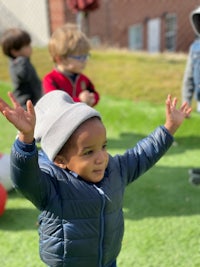 a young boy in a blue jacket with his hands raised in the air