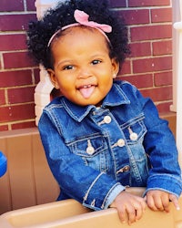 a little girl in a denim jacket sitting in a play yard