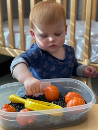 a baby is playing with pumpkins in a plastic container